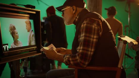 el director mira la pantalla y la compara con el guión gráfico mientras filma una película de éxito de taquilla. escena de pantalla verde con actores interpretando papeles. en el set del estudio de cine, un equipo profesional hace una película de alto presupuesto