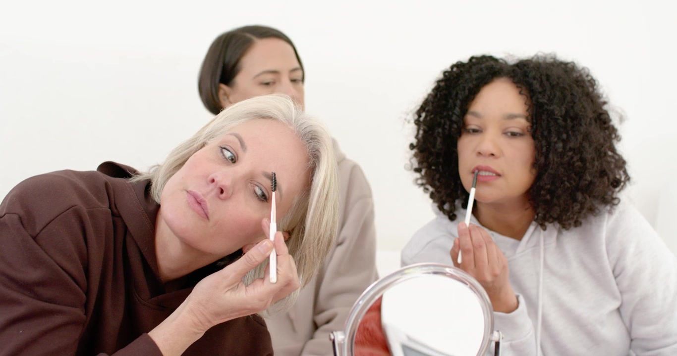 Senior woman with two women on bed reacting to hands choosing palettes testing colors filling brows