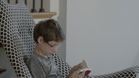 A-young-boy-quietly-reads-a-book-in-a-stylish-chair-at-home