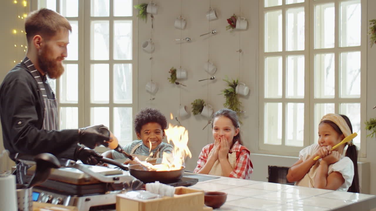 возбужденные дети смотрят, как шеф-повар фламбирует еду на кулинарном уроке.