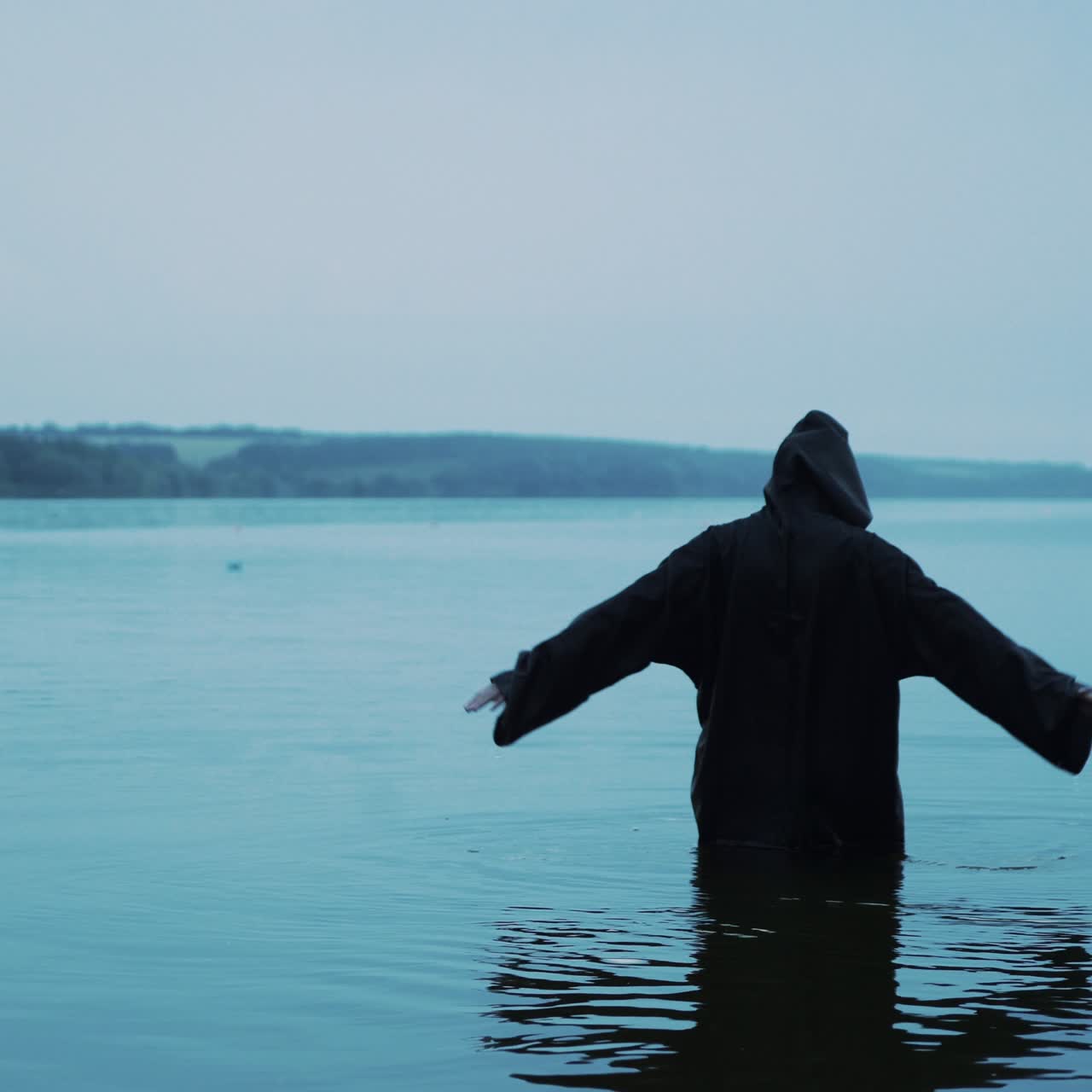 Evil witch in black cloak with hood in the river. Divination by the water. Halloween costume.