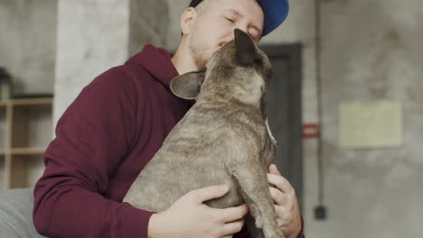 hombre pelirrojo con barba y gorra con su perro bulldog encima de las piernas