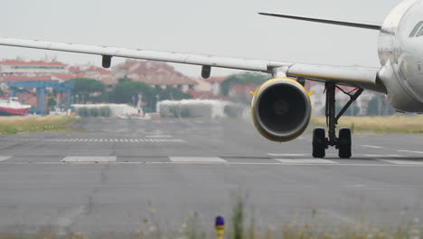 close-up view of airplane wing and engine on runway, showcasing aircraft details and airport facilities in the background, shot in slow motion