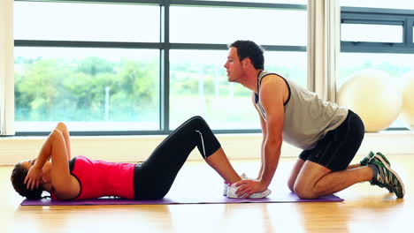 entrenador guapo apoyando a una mujer joven haciendo abdominales
