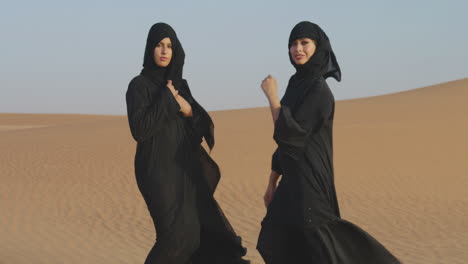 dos hermosas mujeres musulmanas con hiyab posando en un desierto ventoso y mirando la cámara 1