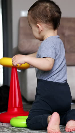 cute little boy plays on the floor assembling the pyramid. black cat sits at backdrop watching the baby. vertical video