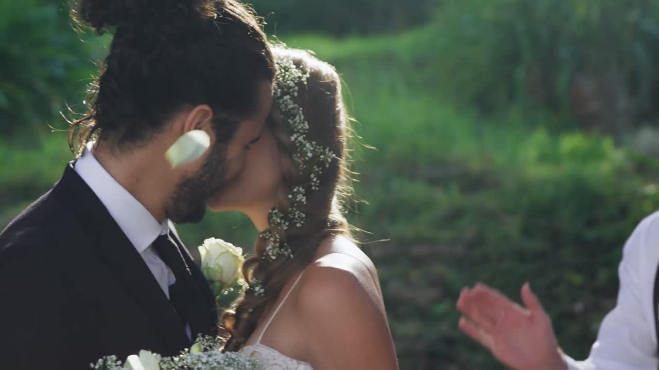 Sposi che si baciano e sullo sfondo gli invitati lanciano petali 4K