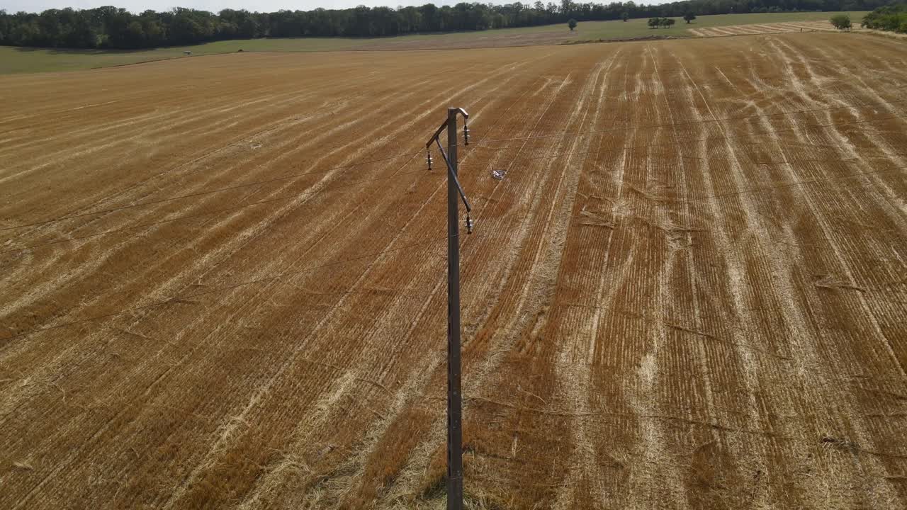 Droneoptagelse trækker sig tilbage fra en betonmast i Frankrig over tørre traktorspor på en landbrugsmark.