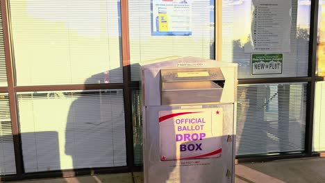 woman votes by casting mail-in ballot letter in slot at voting booth with offical ballot drop box sign for democratic government election in presidential race