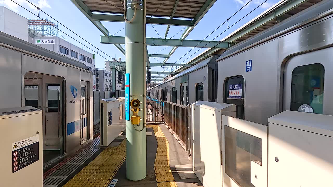 A train arrives and departs at a Tokyo station, showcasing urban transportation. Bright daylight illuminates the modern platform
