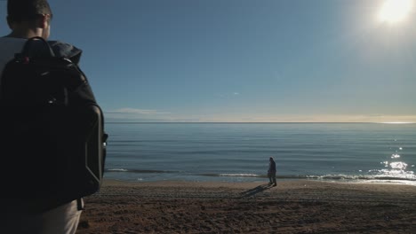 backpacker looking at the beach, drone moving forward with people passing by