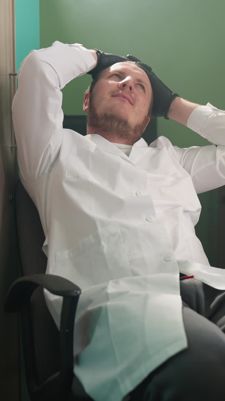 색 실험실 코트를 입은 편안한 기술자가 의자에 기대어, 머리 뒤에 손을 고, 실험실 환경에서 전자 부품과 함께 일하는 것에서 휴식을 취하는 중간 시각