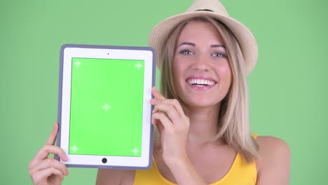 fotografía de estudio de una joven turista sonriendo y mostrando una tableta digital con espacio de copia contra un fondo verde
