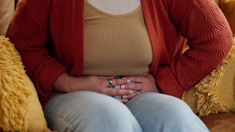 woman holding her stomach in pain while sitting on a couch