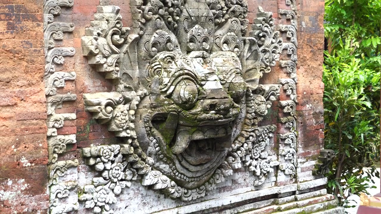 Artigianato artistico in pietra di un rilievo di leone mitologico su parete rossa. Tempio di Ubud, zoom indietro