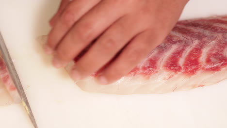 chef cutting meat of fresh raw fish in slow motion for sushi making in a japanese restaurant - high angle shot, close up