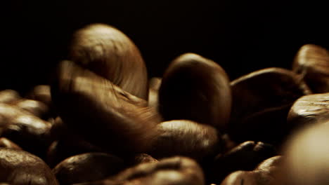 close camera movement through falling fresh coffee beans into a pile of beans laying on a wooden surface