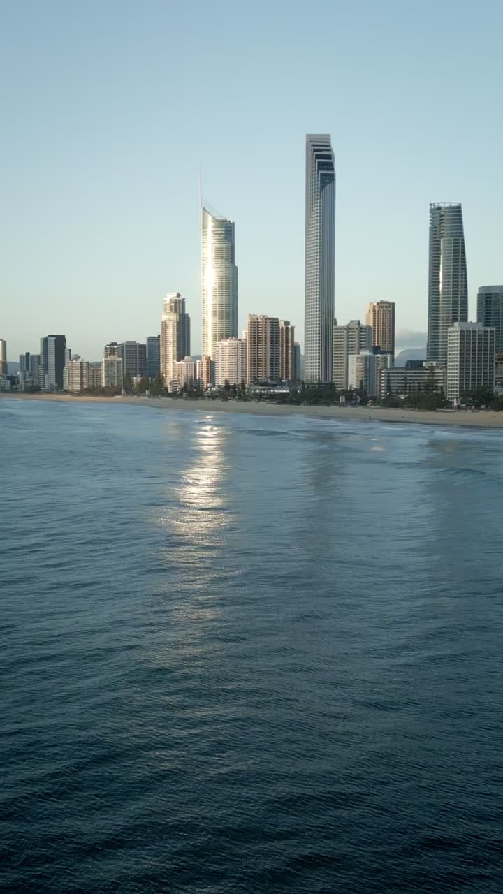 Vertical drone flying backwards out to sea with Surfers Paradise skyline, Gold Coast Queensland Australia. Dramatic ocean perspective showcasing iconic beachfront and coastal city lifestyle paradise