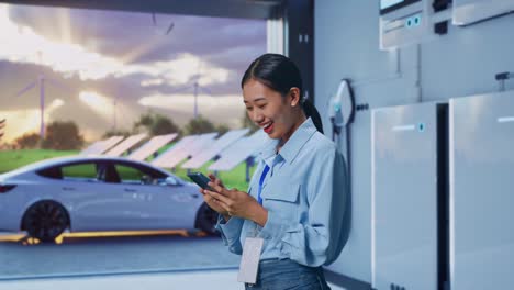 Side View Of Asian Female With Her Smartphone With Home Energy Storage System In a Modern Garage, Checking On Her Smartphone With Meditation