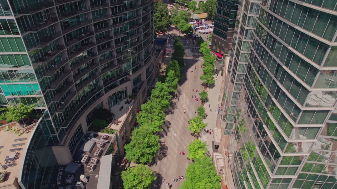 Uma tomada aérea épica sobrevoando edifícios na Peachtree Street coberta de árvores durante um evento de urbanismo do Streets Alive em Atlanta, com ciclistas e pedestres aproveitando um dia de verão ensolarado na cidade
