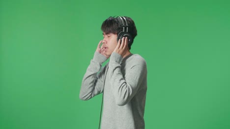 side view asian man listening to music with headphones and dancing in the green screen studio