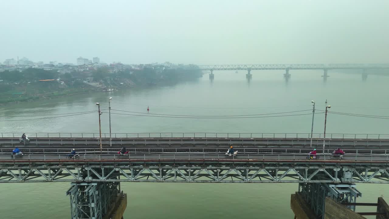 The Long Biên Bridge in Hanoi, Vietnam, shown against a misty, polluted sky. Motorbikes crossing the historical bridge in the capital of the country.