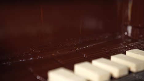 bars of milky sweets being deepened into a thick layer of black chocolate. delicious flow of chocolate falling onto the desserts on the conveyor line. chocolate candies production close up.