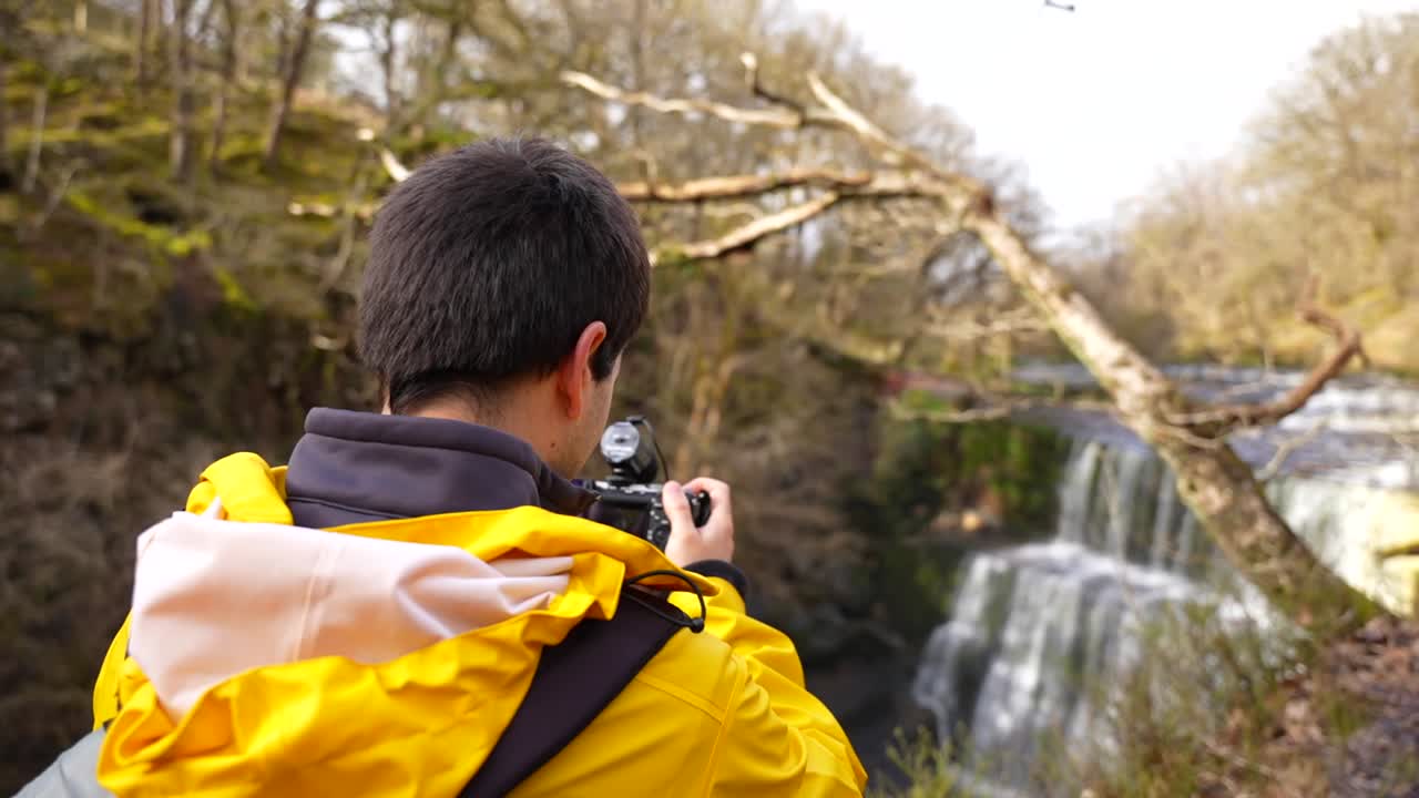 una toma trasera de un hombre filmando la cascada sgwd isaf clun-gwyn en el parque nacional brecon beacons, gales