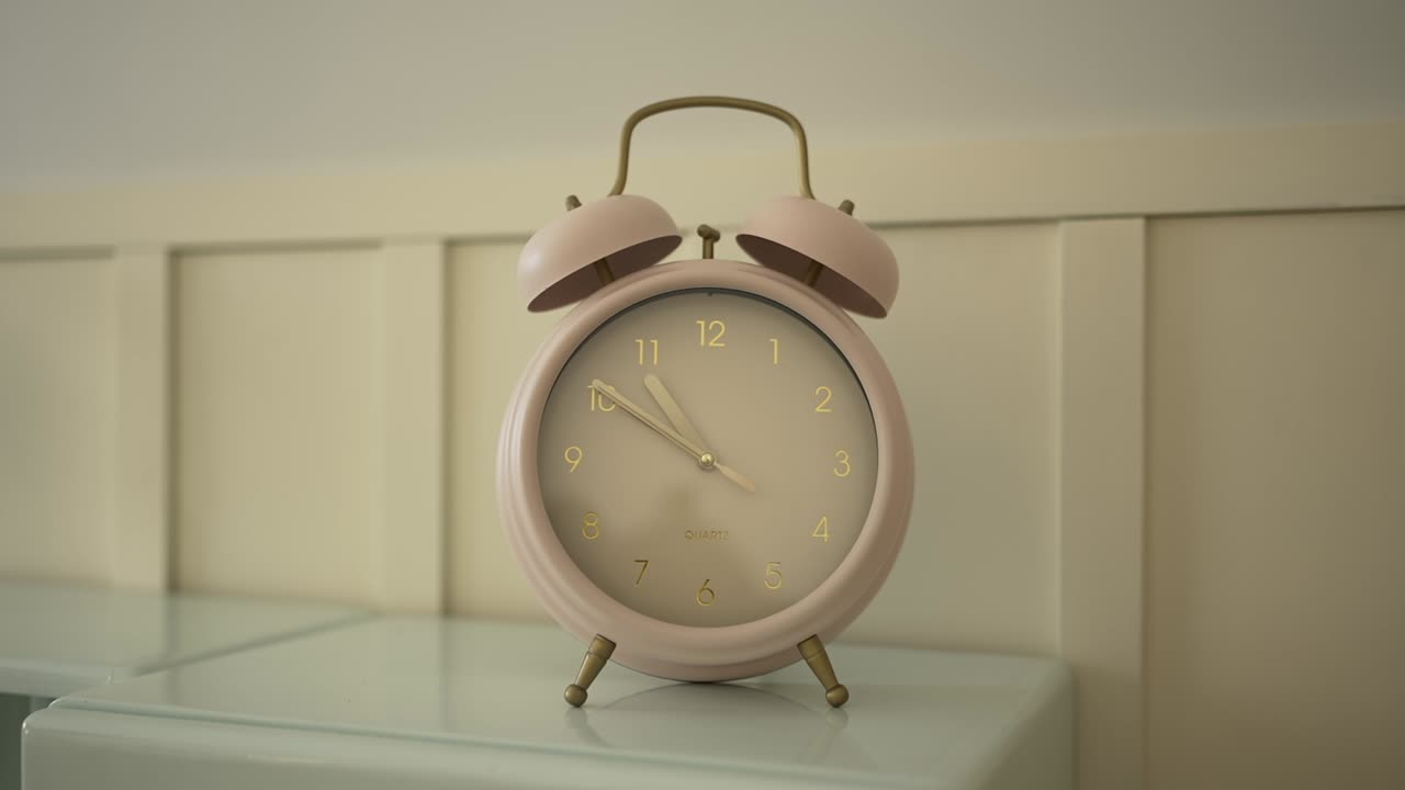 close up of pale pink retro alarm clock on bedside table in natural light