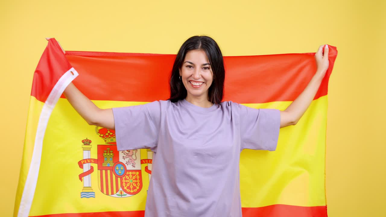 Glückliche Frau, eingewickelt in spanische Flagge, auf gelbem Hintergrund