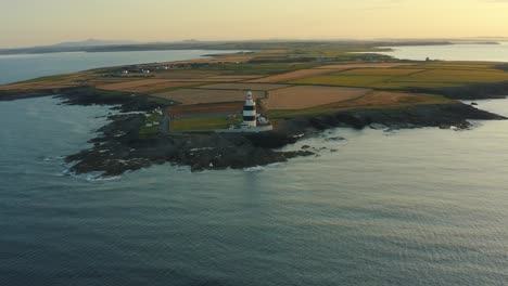 Aerial-view,-sunrise,-high-pan-left,-Hook-Lighthouse-is-situated-on-Hook-Head-at-the-tip-of-the-Hook-Peninsula-in-Co-Wexford,Ireland,-oldest-lighthouse-in-the-world,-was-built-in-the-12th-century