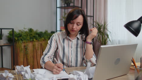 sad young woman working at home office crumples throwing heets of paper with bad ideas and mistakes