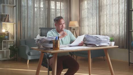 hombre gordo asiático pensando entonces tomando nota mientras trabaja con documentos en la oficina