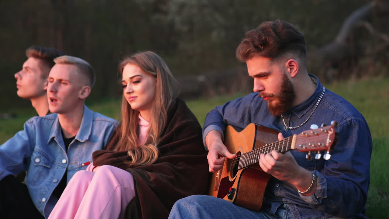 Friends Playing Guitar by Campfire at Sunset