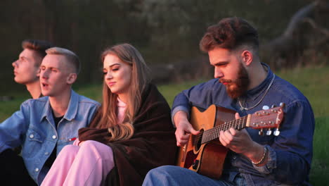 friends playing guitar by campfire at sunset