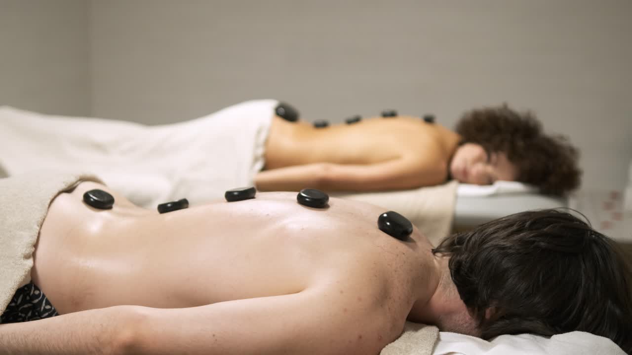 Masseuse gently placing a warm stone on a client's back during a relaxing massage session