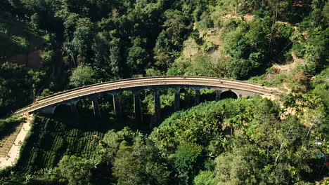 Aerial-of-famous-nine-arch-bridge-in-Ella,-Sri-Lanka-with-blue-train