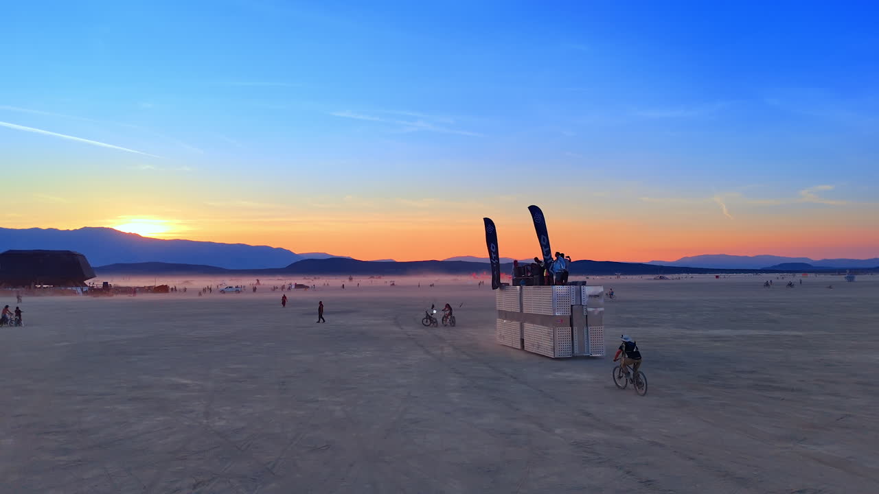 Following a silver rectangular platform with people on top moving by the desert. Progress of Burning Man festival in the Black Rock Desert