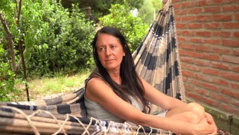 mujer caucásica de unos 50 años relajándose en una hamaca fuera de la casa