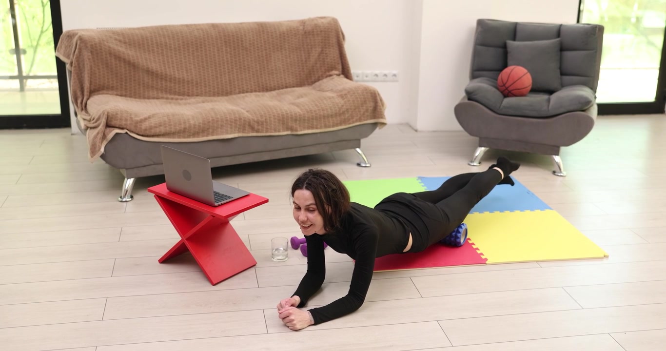 Woman lies on colorful mat on floor using foam roller under legs