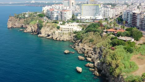 aerial drone circling cliffs surrounded by the blue mediterranean sea and large residential buildings in antalya turkey on a sunny summer day