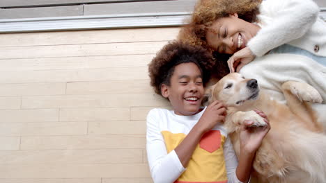 happy african american mother and son lying on floor, with their pet dog, copy space, slow motion