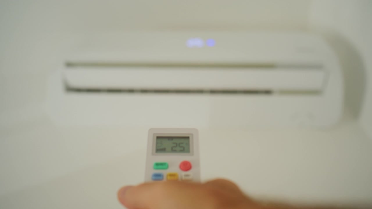 Mano che tiene un telecomando, regolando le impostazioni di temperatura e raffreddamento su un'unità di condizionamento d'aria a parete