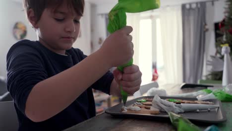 niño caucásico decora galletas de jengibre navideñas en casa, usando una manga pastelera