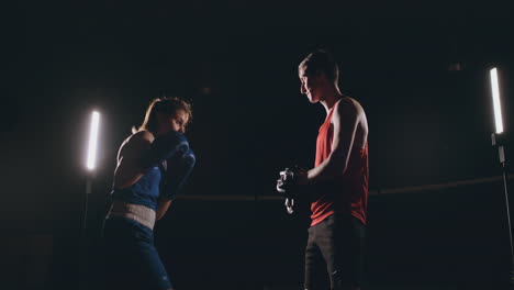 Kickboxer-Mujer-Atleta-Entrenador-De-Kickboxing-Entrenamiento-Femenino-Fitness-Amigos-Boxeo-Puñetazos-Enfoque-Guantes-Disfrutando-De-Intenso-Ejercicio-Juntos-En-El-Gimnasio-De-Cerca