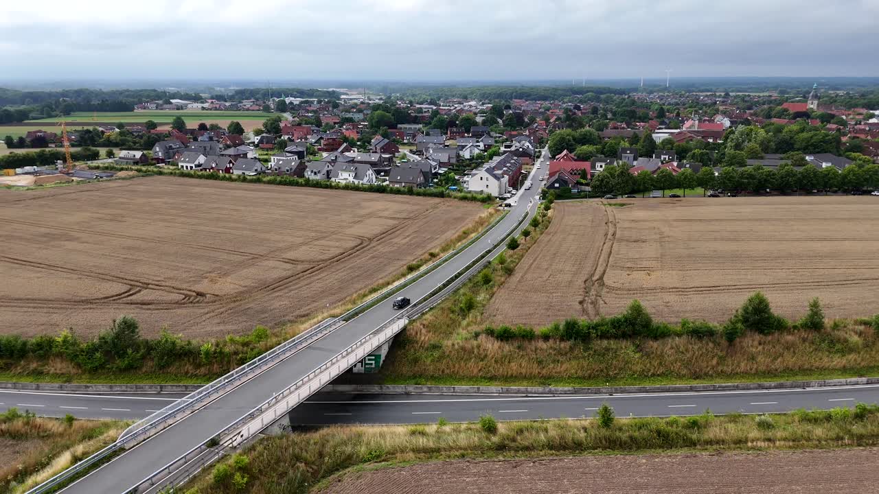 Vehicles on Rural road below bridge leading to American city in Wisconsin. Summer day with clouds at sky. Aerial lateral wide shot