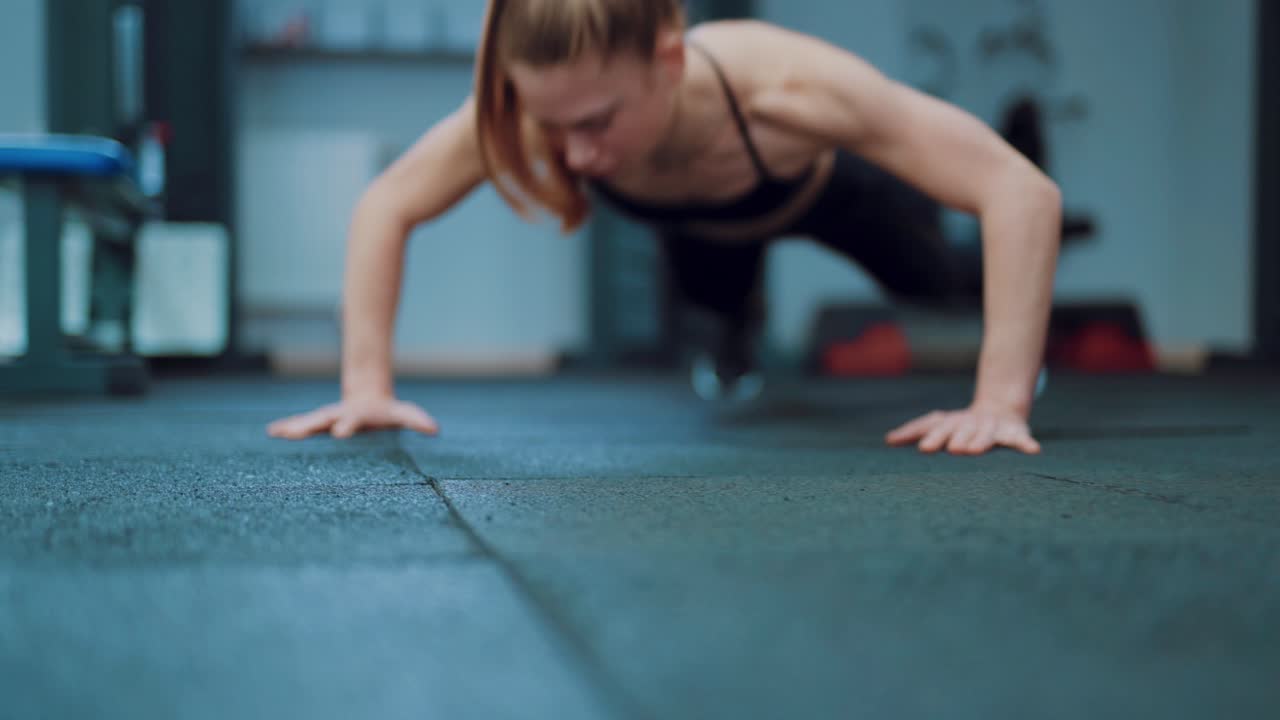 A strong woman with a ponytail push up from the floor in the gym. Blurred background. Camera motion forward