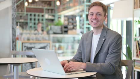 young businessman with laptop smiling at camera