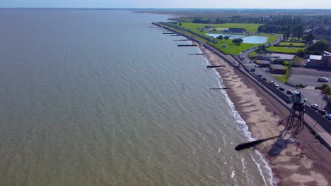 Aerial-Drone-View-of-Dovercourt-Beach,-Lighthouse,-Causeway,-and-Colorful-Beach-Huts-in-the-Distance