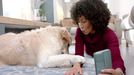 happy biracial woman with golden retriever dog using smartphone at home, slow motion